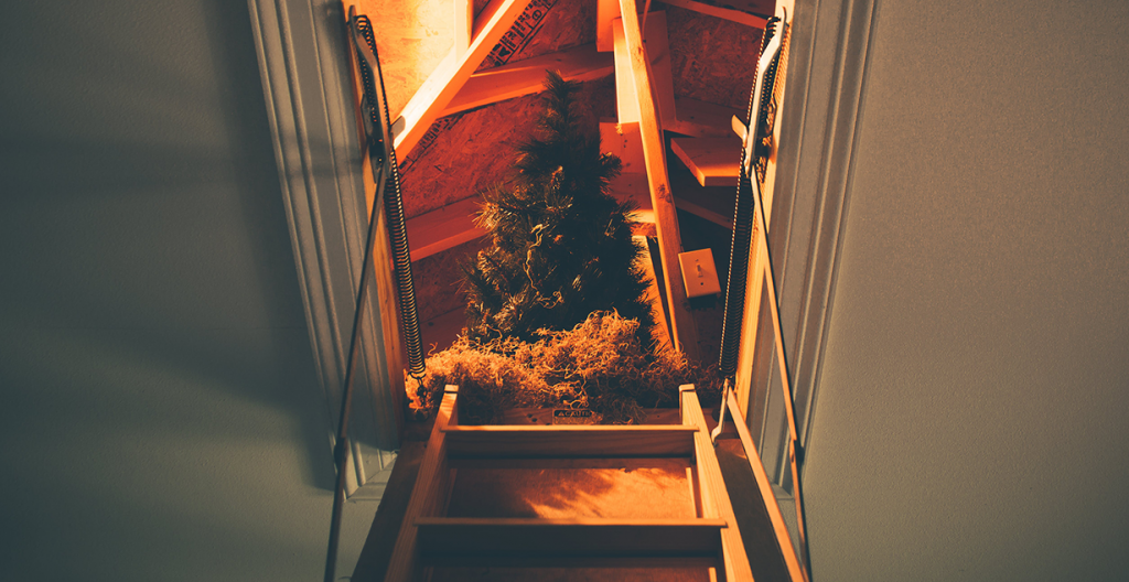 an upright artificial Christmas tree is at the top of a loft space, which has wooden stairs leading up to it. 